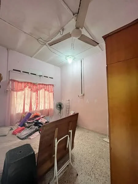 Bedroom features: pink painted walls, exposed beams ceiling, ceiling fan, light fixture, window with sheer curtains, bed with bedding, wooden wardrobe, folding table, standing fan, tile flooring.