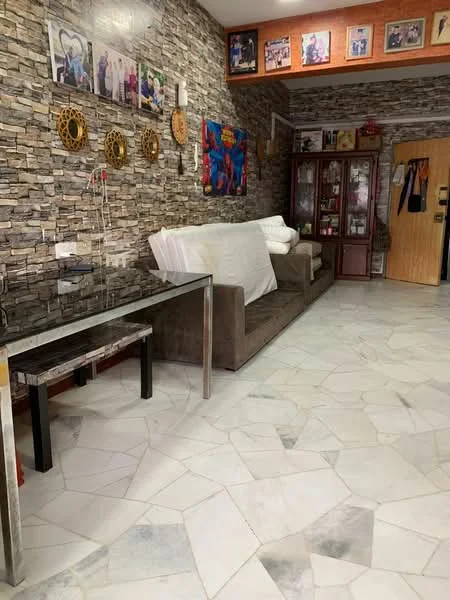 Living features: grey fabric sofa, glass coffee table, stone feature wall with mixed textures, marble flooring, wooden door, decorative wall art, framed photographs on wall, cabinets with glass doors; style: modern.