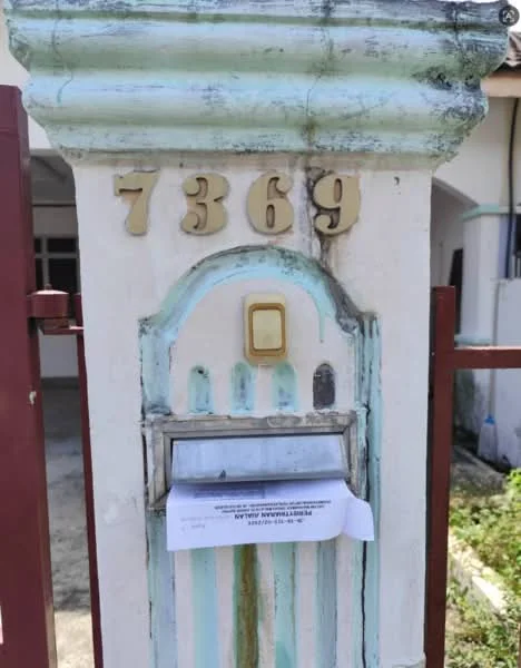 Exterior features: mailbox with decorative design, weathered paint with blue and white colors, house number 7369 displayed, metal gate, overgrown grass in front, visible pathway; style: traditional.