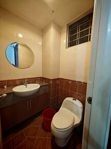 Bathroom features: single-sink vanity with grey countertop, round mirror, one-piece toilet, tile cladding on walls, brown tiled flooring, window with metal grille, wooden cabinet under sink, red plastic bucket.