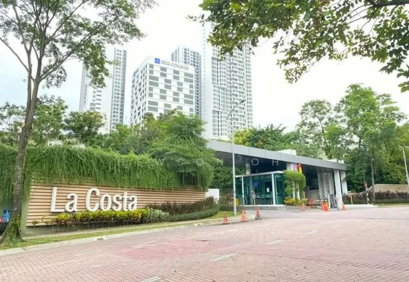 Exterior type: gated community; features: modern entrance gate, landscaped greenery, signage with 'La Costa', paved driveway, surrounding trees, multi-storey residential buildings in background, visible parking area, security features at entrance; style: modern.