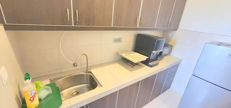 Kitchen features: single-bowl stainless-steel sink, chrome pull-down faucet, laminate countertop, brown cabinetry, white tiled backsplash, built-in water dispenser, freestanding fridge, dish rack, cleaning supplies on countertop; style: modern.