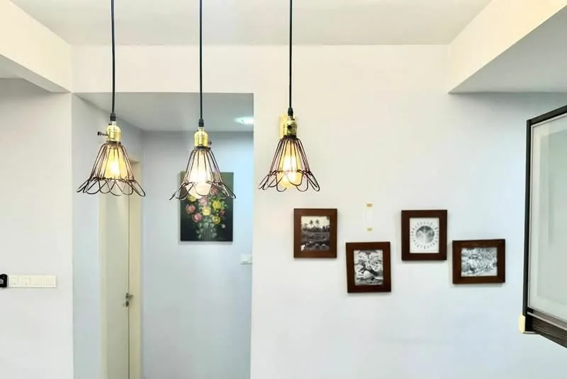 Room features: white painted walls, 3 pendant lights with wire cages, framed artwork on walls, light switch, doorway leading to another room; style: modern.