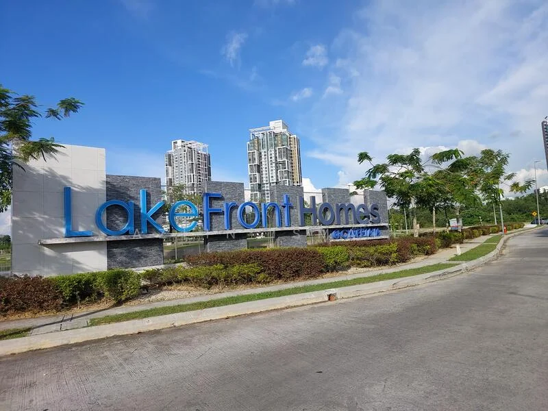 Exterior features: signage with blue lettering, landscaped garden with shrubs, paved driveway, surrounding trees, modern high-rise buildings in background, clear blue sky; style: modern.