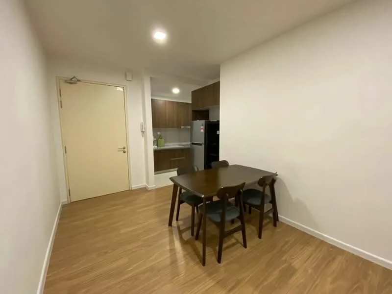 Dining features: wooden dining table, 4 dining chairs, light wood flooring, white painted walls, recessed downlights, open layout to kitchen, doorway to hallway, kitchen visible in background; style: modern.