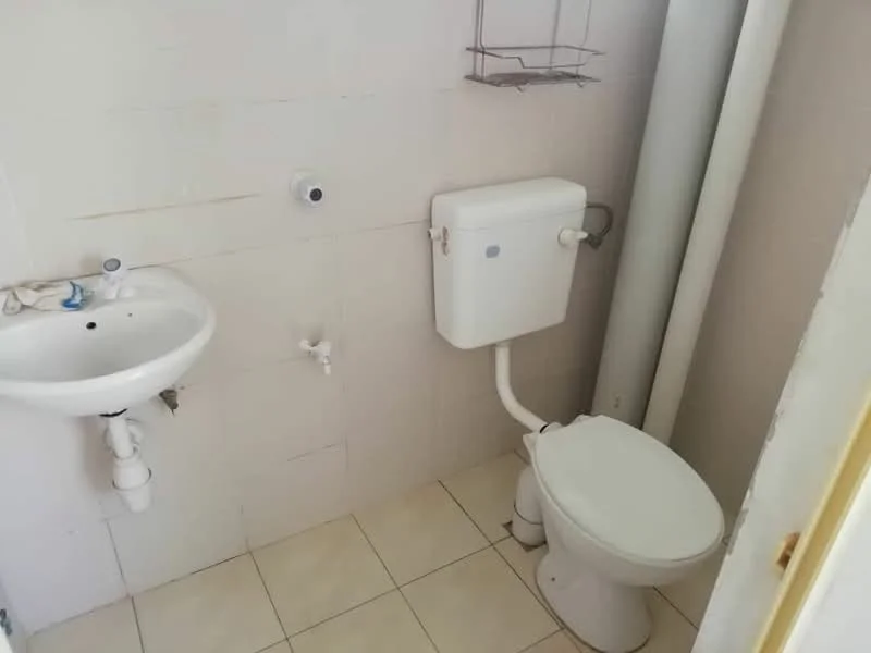 Bathroom features: white ceramic toilet, one-piece toilet, white sink, wall-mounted sink, chrome faucet, white tiled walls, cream tiled flooring, toilet tank, exposed plumbing, shelf above sink.