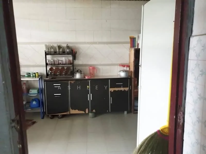 Kitchen features: white tiled walls, grey tiled flooring, black cabinetry with peeling paint, metal shelving unit with dishes, stainless-steel pot on stove, plastic containers, kitchen utensils, broom visible in corner.