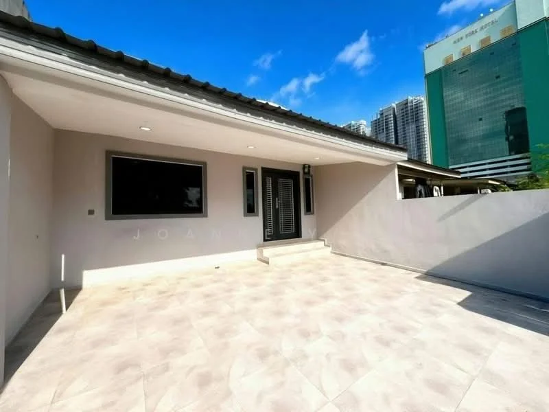 Exterior type: detached bungalow; features: grey painted facade, flat roof, large windows, stone-paved patio, steps leading to entrance, surrounded by low walls, urban backdrop with high-rise buildings, clear blue sky; style: modern.