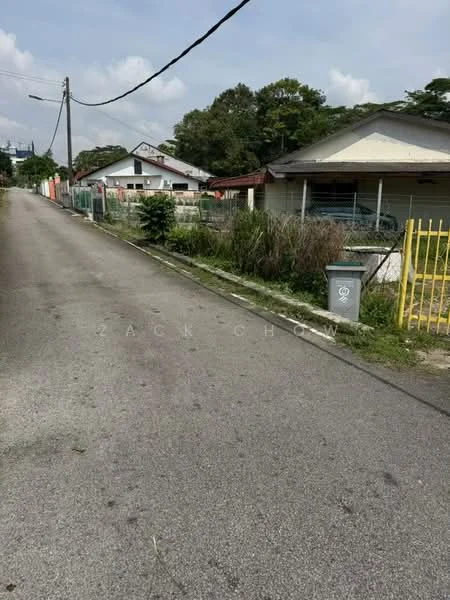 Exterior features: paved road, residential houses, fenced properties, overgrown grass, utility pole, yellow gate, garbage bin, trees lining the street.