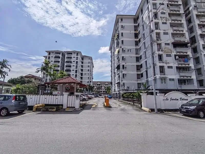 Exterior type: low-rise apartment block; features: white painted facade, multiple storeys, balconies visible, landscaped garden area, manicured lawn, paved driveway, parking spaces, security guardhouse, surrounded by greenery, signage at entrance; style: modern.