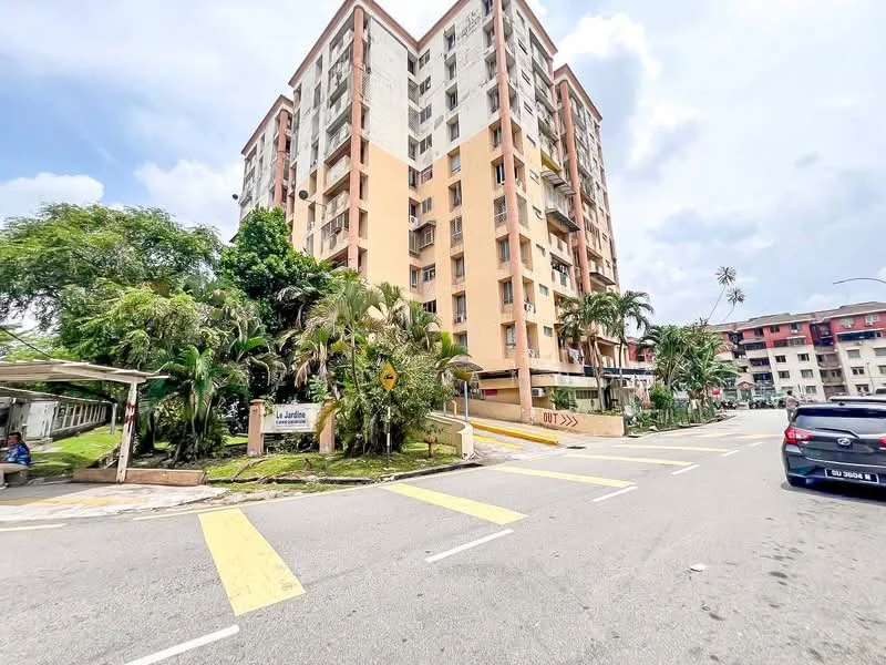 Exterior type: low-rise apartment block; features: pink painted facade, green landscaping with palm trees, manicured lawn, multiple balconies, parking area visible, surrounded by greenery, street view, sidewalk, road with yellow pedestrian crossing; style: modern.