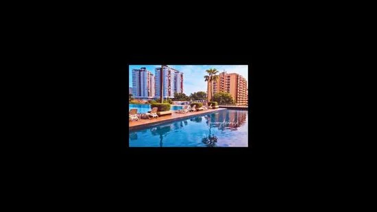 Exterior type: swimming pool deck; features: infinity pool, pool deck with loungers, surrounding palm trees, multiple high-rise buildings in background, clear blue water, sunny weather, outdoor seating area; style: modern.