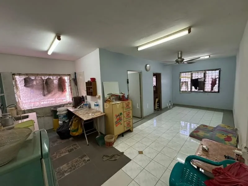 Kitchen features: white painted walls, grey tiled flooring, ceiling fan, double-bowl stainless-steel sink, wooden cabinetry, kitchen countertop, refrigerator, washing machine, window with metal grille, dining table, plastic chair, area rug, wall clock. Room features: white painted walls, grey tiled flooring, window with metal grille, doorway to hallway.