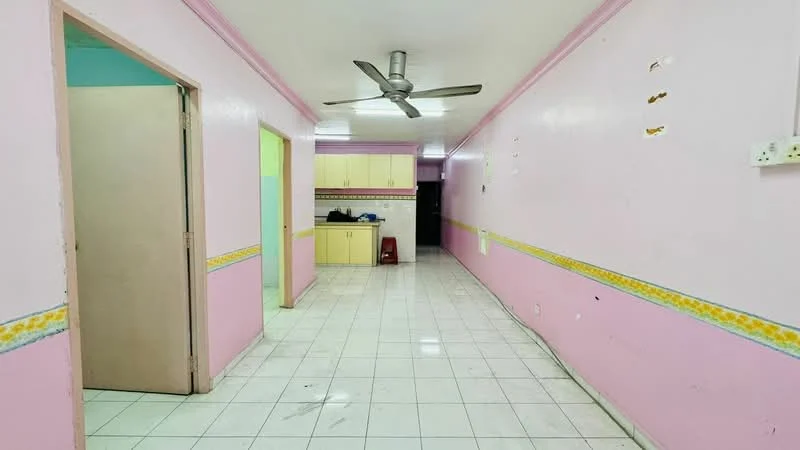 Room features: pink painted walls, white tiled flooring, ceiling fan, doorway leading to another room, doorway leading to kitchen, decorative wall trim with floral pattern, built-in cabinetry in kitchen area, open layout, light fixtures on ceiling.