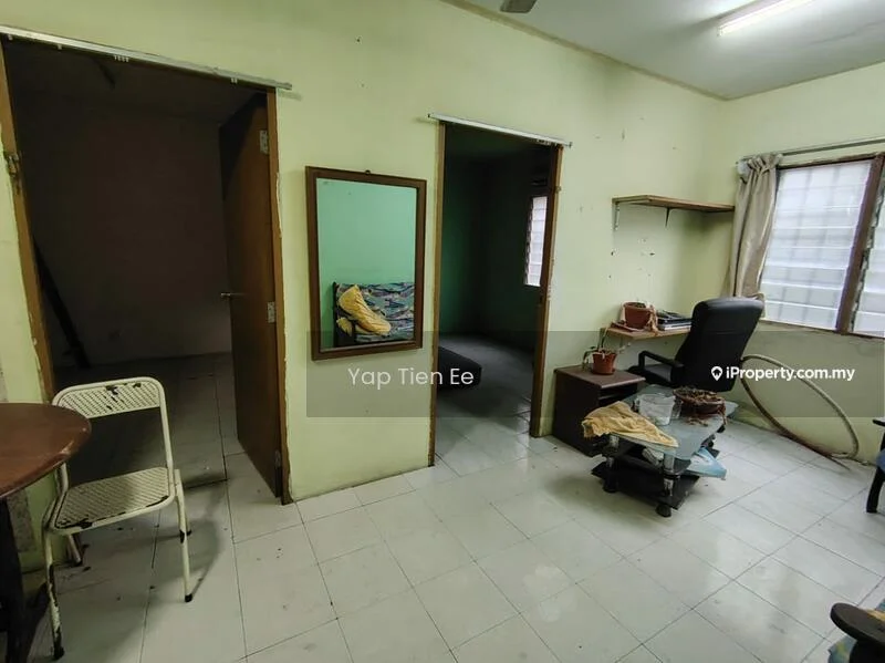 Room features: white painted walls, tile flooring, window with sheer curtains, wooden door, mirror on wall, desk with chair, small table, clothes on chair.
