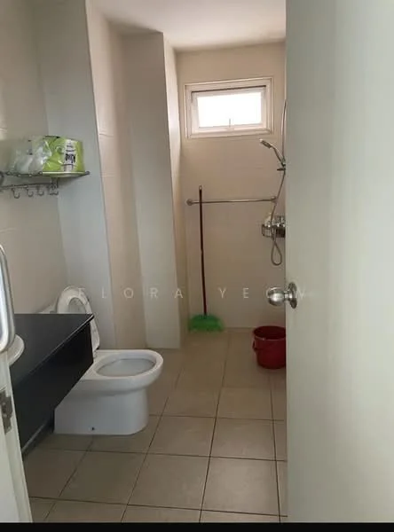 Bathroom features: white ceramic toilet, single-sink vanity with dark cabinet, shower area with handheld shower, tile flooring, light beige wall tiles, window for natural light, towel rack, cleaning supplies on shelf, red bucket, green mop, mirror above vanity.