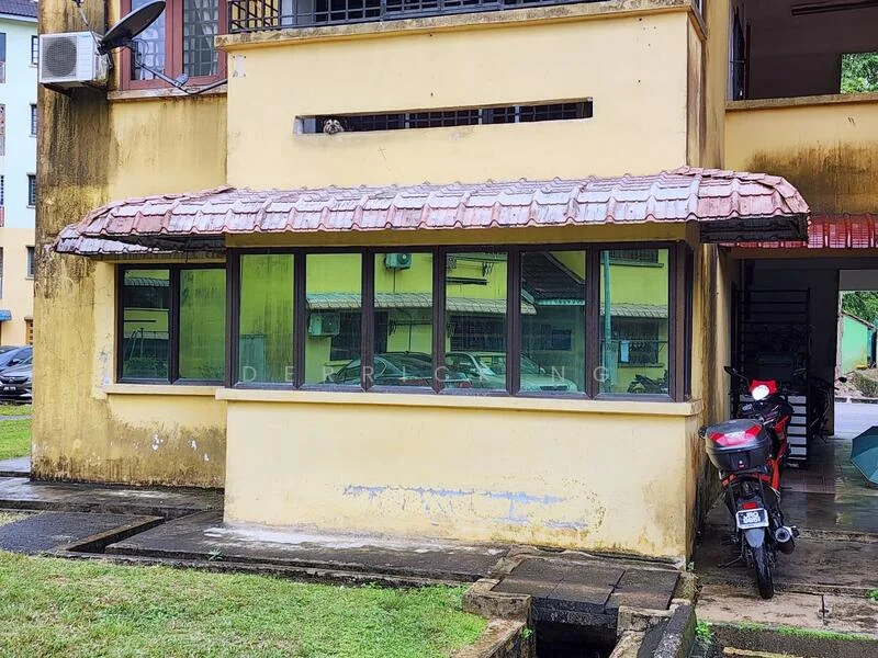 Exterior type: low-rise apartment block; features: yellow painted facade, red tiled roof, large windows with green frames, ground floor unit, visible parking area, manicured lawn, concrete pathway, air conditioning unit on wall; style: modern.