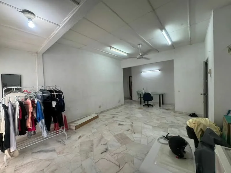 Room features: marble flooring, white painted walls, exposed ceiling with fluorescent lights, ceiling fan, clothes rack with various clothing, desk with chair, doorway leading to another room, empty corner with a helmet; style: minimalist.