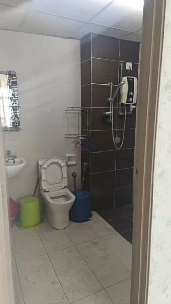 Bathroom features: white ceramic toilet, chrome toilet paper holder, white sink with chrome faucet, shower area with glass partition, handheld shower head, wall-mounted shower control, dark brown tile wall, light-colored tile flooring, mirror above sink, metal towel rack, plastic stool in green, blue bucket.