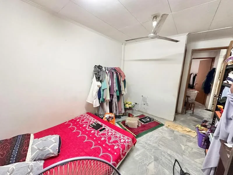 Bedroom features: red patterned bedspread, queen-size bed, ceiling fan, marble flooring, white painted walls, wooden wardrobe, clothes rack with hanging clothes, decorative rug, small table, basket, laundry on the floor.