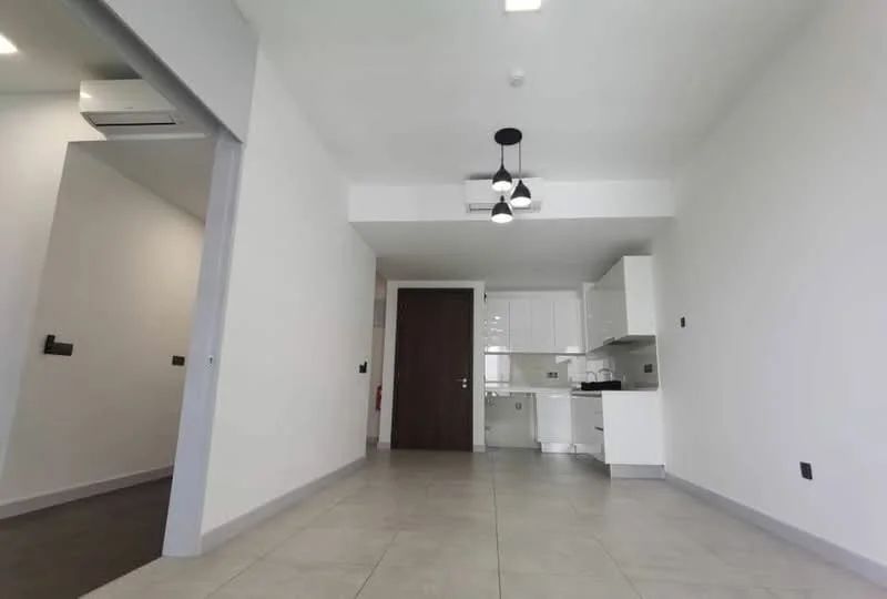 Room features: white painted walls, grey tiled flooring, recessed downlights, ceiling light fixture with multiple bulbs, wall-mounted air conditioning unit, kitchen cabinetry in white, stainless-steel sink, countertop, open layout, door leading to another room, window, fire alarm, smoke detector; style: modern.
