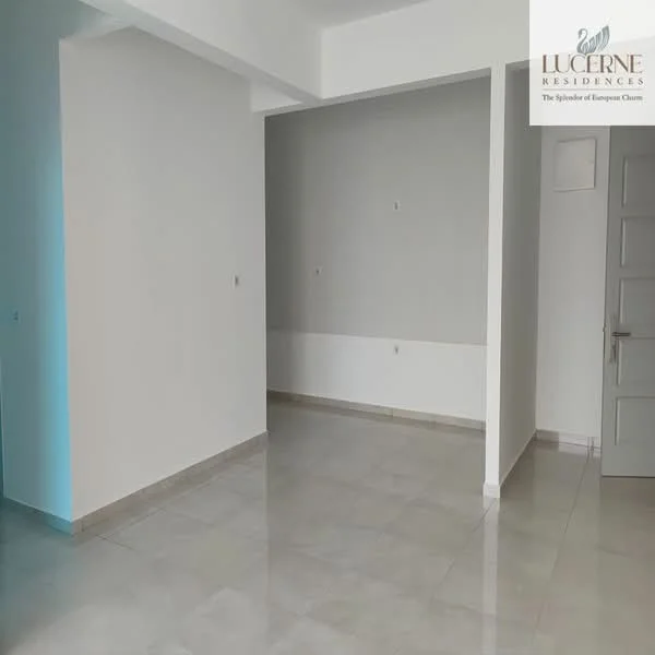 Room features: white painted walls, grey accent wall, glossy tile flooring, recessed ceiling, single door, corner with no visible furniture, natural light from windows, neutral color palette; style: modern.