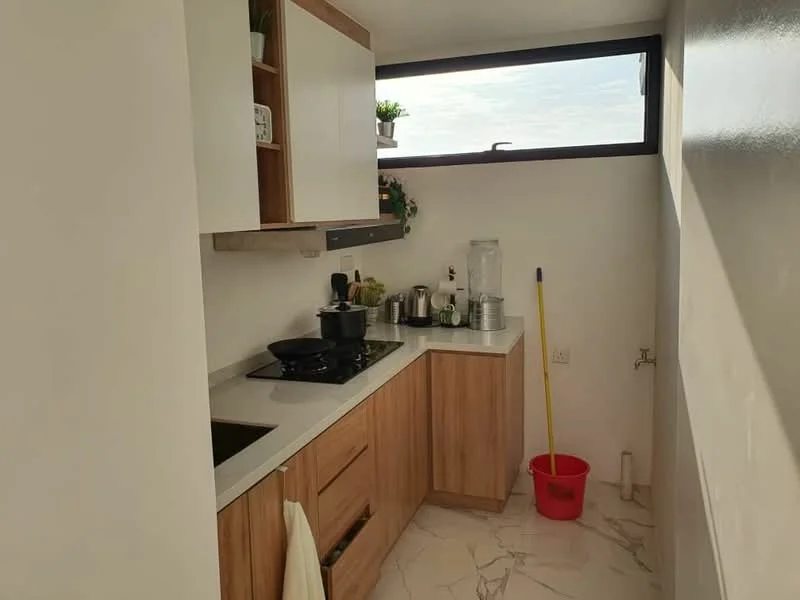 Kitchen features: white cabinetry, wooden lower cabinets, black gas stove, stainless-steel sink, white countertop, marble tile flooring, window with natural light, decorative plants on shelf, kitchen utensils, cleaning supplies, water dispenser, red bucket; style: modern; view: sky.