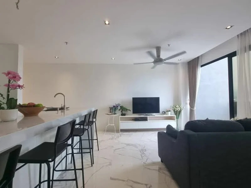 Living features: sofa in dark grey fabric, coffee table, wall-mounted TV, TV console in white, 5-blade ceiling fan with light, large windows with sheer curtains, marble tile flooring, decorative plants in ceramic pots, open-plan layout with kitchen, bar stools at kitchen counter, kitchen island with white countertop; style: modern.