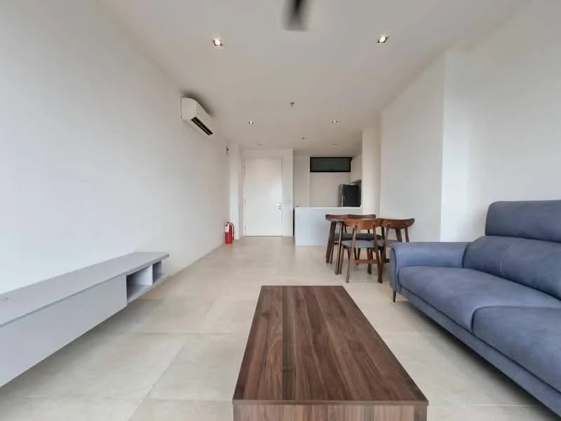 Living features: light grey fabric sofa, wooden coffee table, wall-mounted TV console, recessed downlights, wall-mounted split AC, cream painted walls, large windows, tile flooring; style: modern. Kitchen features: open kitchen layout, black countertop, built-in cabinetry, stainless-steel fridge, microwave, induction hob, extraction hood; style: modern.