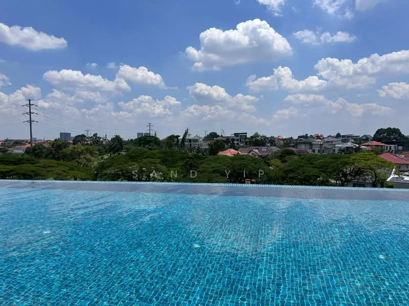 Exterior type: swimming pool deck; features: infinity pool, blue mosaic tile pool surface, surrounded by greenery, city skyline in background, clear blue sky, clouds, landscaped area around pool; style: modern.