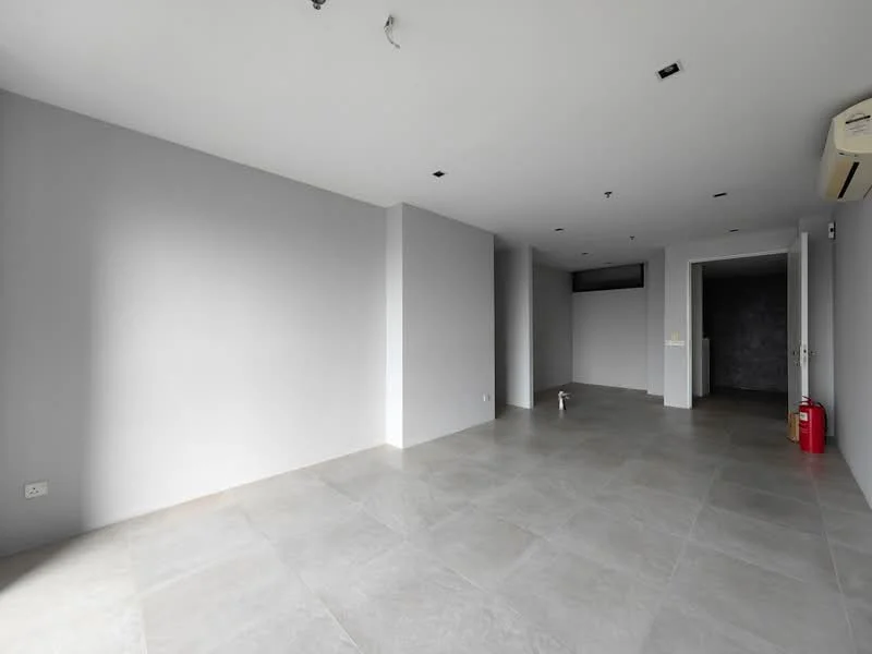 Room features: grey painted walls, polished concrete flooring, recessed downlights, floor-to-ceiling windows, air conditioning unit, fire extinguisher, open layout, no visible furniture or decor; style: modern.