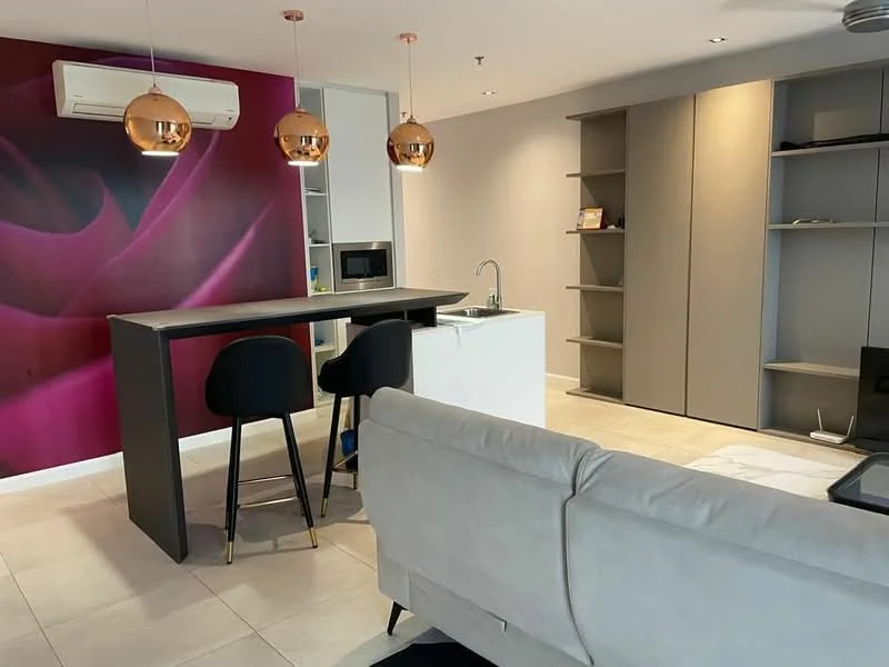 Living features: grey sofa, black bar stools, kitchen island with seating, white countertop, built-in shelving unit, wall-mounted air conditioning unit, pendant lighting with copper finish, pink accent wall with floral design, tile flooring, recessed lighting, microwave, open layout; style: modern.