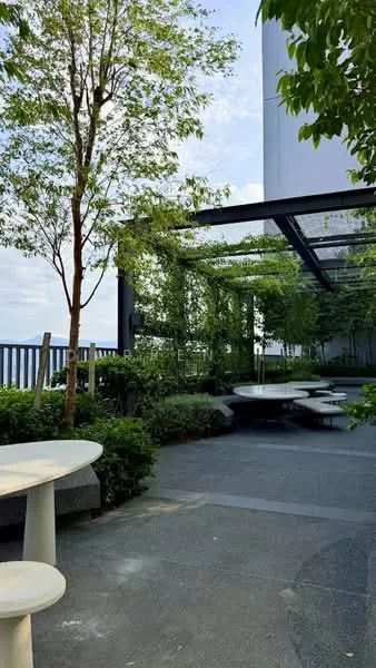 Exterior type: landscape garden; features: outdoor seating area with circular tables, landscaped greenery with shrubs, trees providing shade, paved flooring, pergola structure with climbing plants, railings along the edge, open sky view; style: modern.