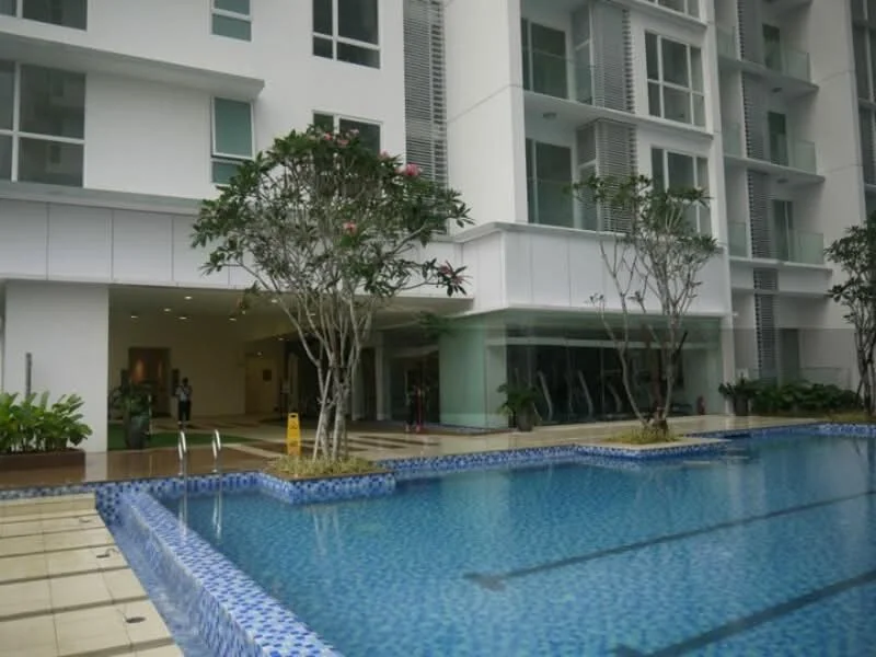Exterior type: high-rise condominium; features: swimming pool with tiled edge, pool deck with loungers, landscaped garden with plants, glass facade on building, entrance lobby visible, manicured lawn, trees surrounding the pool area; style: modern.
