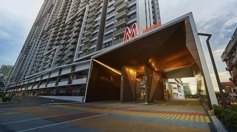 Exterior type: high-rise condominium; features: modern facade with geometric design, glass curtain wall, metal cladding, double-volume main lobby, covered entrance, paved driveway, landscaped garden area, signage with letter 'M', parking area, surrounded by urban environment; style: modern.