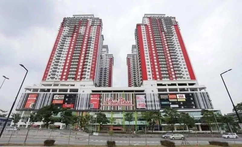 Exterior type: high-rise condominium; features: red and white facade, glass curtain wall, multiple storeys, commercial space at ground level, manicured landscaping, surrounded by trees, balconies on upper floors, prominent signage on building, parking area visible, urban context with road access; style: modern.
