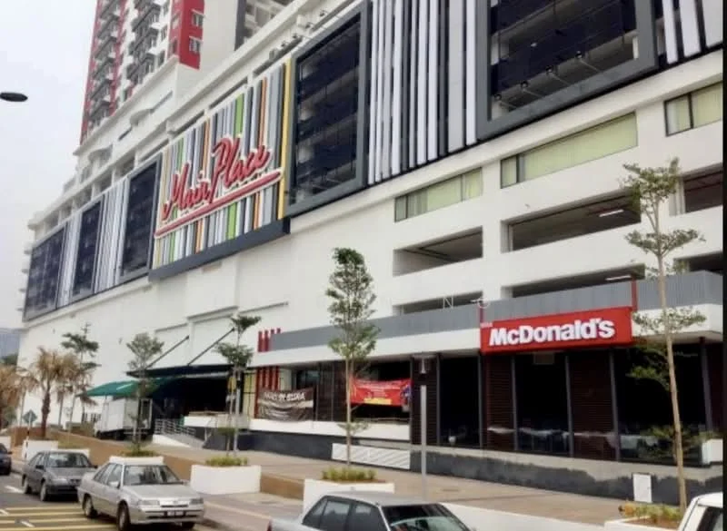 Exterior type: mixed-use development; features: multi-storey building, commercial ground floor, residential units above, glass facade, colorful vertical stripes, awning over outdoor seating area, visible signage for McDonald's, landscaped area with small trees, parking spaces in front, street view with cars, entrance to the building; style: modern.
