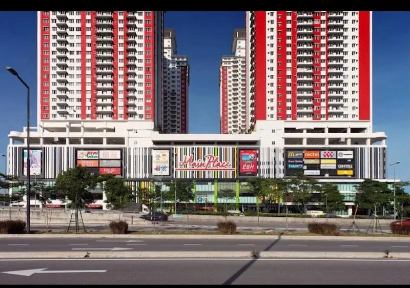 Exterior type: high-rise condominium; features: red and white painted facade, glass curtain wall, multiple balconies, commercial space at ground level, signage for various shops, surrounded by landscaped greenery, paved walkway, urban context with road in front; style: modern.