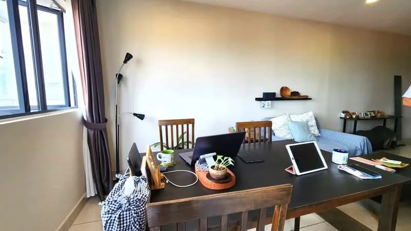 Dining features: wooden dining table, 4 wooden dining chairs, laptop on table, tablet on table, potted plant on table, black and white checkered bag, wall-mounted shelf, decorative items on shelf, grey fabric sofa in background, floor-to-ceiling window, curtains, neutral painted walls, tile flooring; style: modern; view: city.
