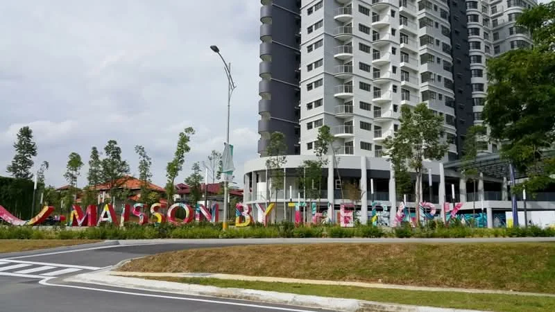Exterior type: high-rise condominium; features: modern facade with glass and concrete, colorful signage, landscaped garden with young trees, surrounding residential buildings, driveway leading to entrance, multiple storeys, balconies visible on upper floors; style: modern.