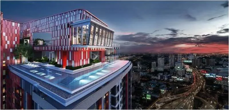 Exterior type: high-rise condominium; features: red and white patterned facade, glass curtain wall, infinity pool, rooftop terrace, outdoor lounge area, landscaped garden on terrace, city skyline view, nighttime lighting, surrounded by urban landscape; style: modern.