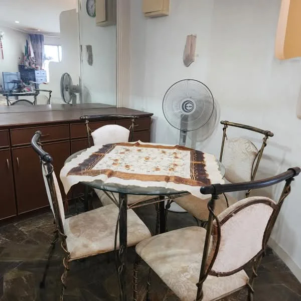 Dining features: round dining table with decorative tablecloth, 4 upholstered dining chairs, metal frame for dining table, ceiling fan, wooden cabinetry in background, stone flooring, wall-mounted clock, neutral wall color.