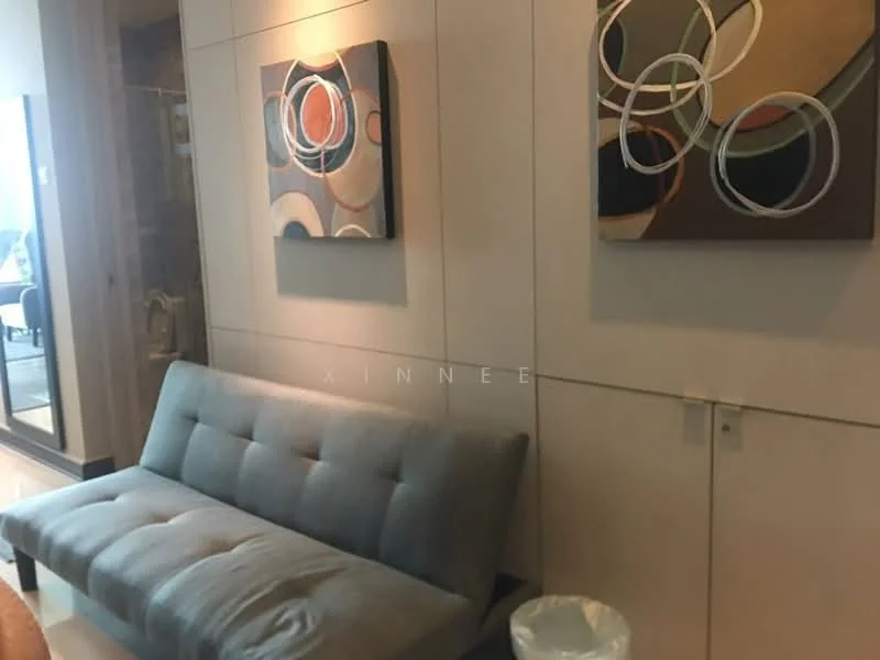Room features: grey fabric sofa, abstract wall art with circular patterns, light-colored wall panels, decorative wall lighting, small waste bin; style: modern.