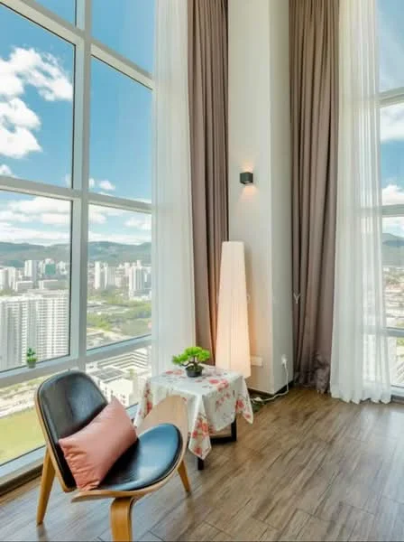 Room features: floor-to-ceiling windows, city view, wooden flooring, light-colored curtains, dark-colored chair, decorative table with floral tablecloth, table lamp, potted plant, wall-mounted light fixture; style: modern; view: city.