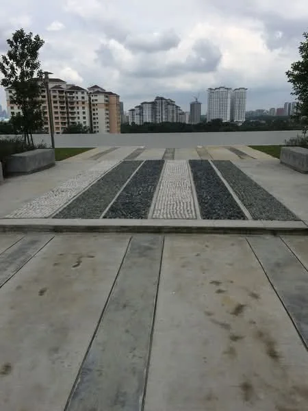 Exterior type: landscape garden; features: paved walkway with stone patterns, concrete surface, surrounding greenery with trees, view of residential buildings in the background, cloudy sky, urban landscape; style: modern.