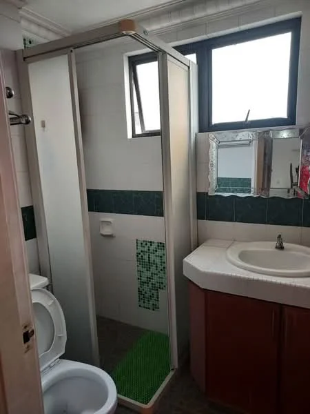 Bathroom features: shower cubicle with sliding door, white toilet, single-sink vanity with countertop, mirror with decorative frame, green mosaic tile backsplash, white tiled walls, dark green tiled accent, window for natural light, light fixture above mirror, flooring with grey tiles; style: modern.
