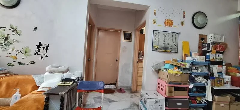 Room features: white painted walls, marble flooring, wooden door, decorative wall art, shelves with various items, stacked boxes, small table with chair, light fixture on wall.
