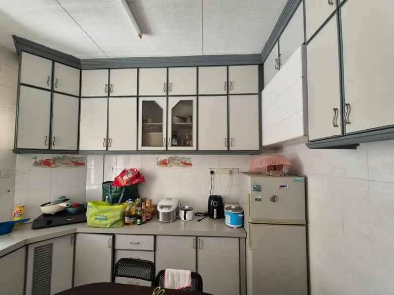 Kitchen features: L-shaped countertop, grey laminate countertop, white upper cabinets with glass inserts, grey lower cabinets, built-in fridge, microwave, electric kettle, toaster, stainless-steel sink, wall-mounted shelves, tile backsplash, white tiled walls, ceiling with textured design, overhead lighting; style: modern.