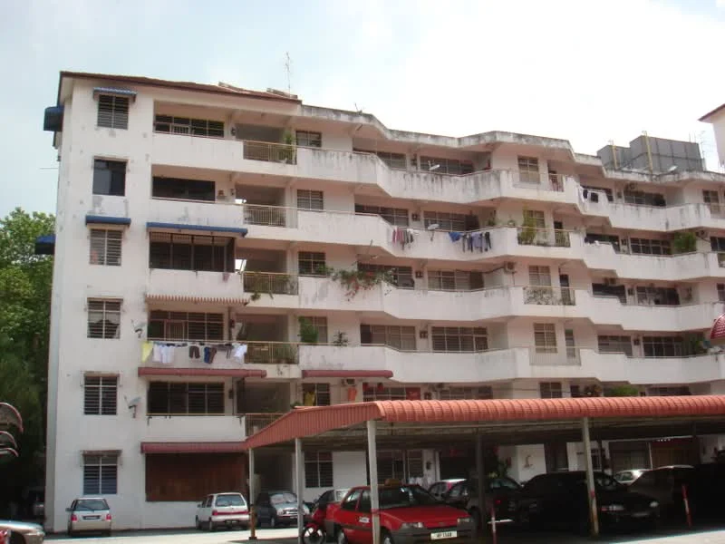 Exterior type: low-rise apartment block; features: white painted facade, multiple balconies with railings, visible laundry hanging on balconies, flat roof, covered parking area, red awning over parking, ground floor parking, surrounded by greenery; style: traditional.