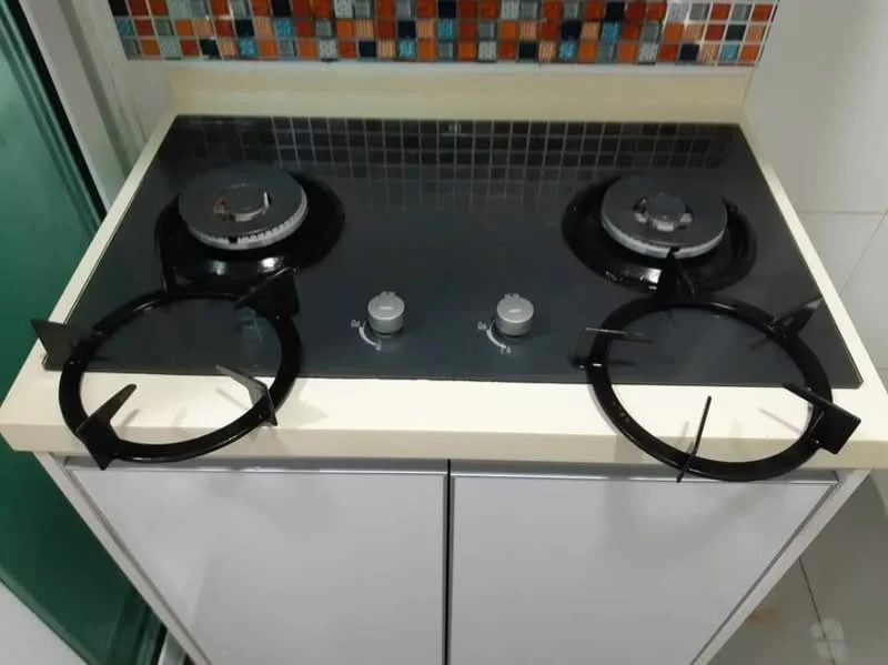 Kitchen features: black gas hob with two burners, stainless-steel knobs, cream countertop, white cabinetry, mosaic tile backsplash with colorful pattern, grey tile flooring; style: modern.